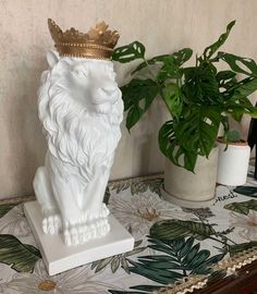 a white lion statue with a crown on it's head next to a potted plant