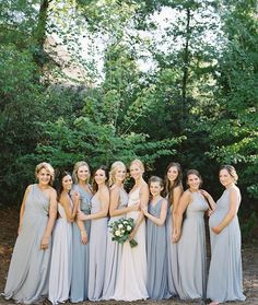 a group of women standing next to each other in front of some trees and bushes