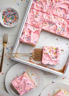 pink frosted cake with sprinkles on white plates and gold utensils