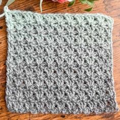 a crocheted square sitting on top of a wooden table next to a flower