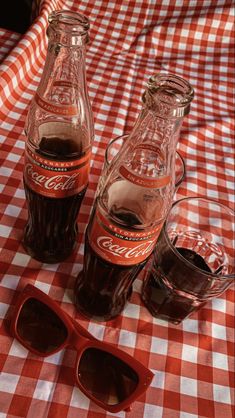 three coca - cola bottles sitting on top of a red and white checkered tablecloth