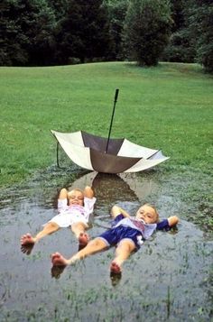 two small children laying in the water with an umbrella over their heads and one is upside down