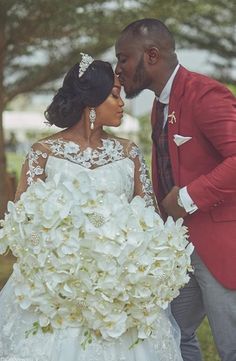 a bride and groom kissing each other in front of trees with white flowers on the bouquet