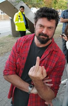 a man with a goatee standing in front of some people and making the peace sign