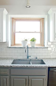 a kitchen with white cabinets and gray counter tops, an open window above the sink