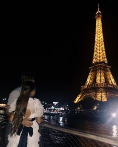 a man and woman standing next to each other near the eiffel tower at night