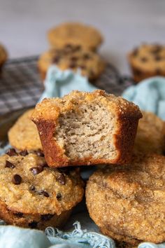 muffins with chocolate chips in the middle on a blue cloth next to other muffins