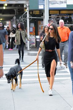 a woman is walking her dog down the street while people walk on the sidewalk behind her