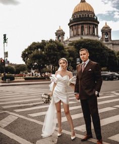 a man and woman standing in the middle of a cross walk with buildings in the background