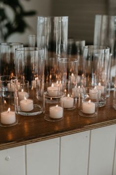 candles are lined up on a table with clear glasses