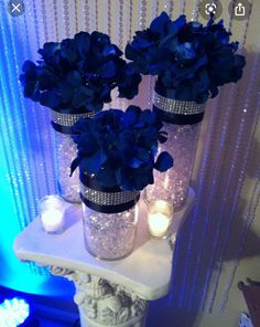 three vases filled with blue flowers sitting on top of a white table next to candles