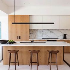 two stools sit in front of an island with marble countertops and wooden cabinets