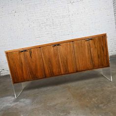 a large wooden cabinet sitting on top of a cement floor next to a white brick wall