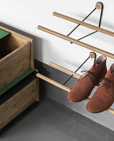 a pair of brown shoes hanging from a wooden rack next to a green box and two drawers