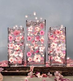 three clear vases with pink flowers in them on a wooden table surrounded by petals