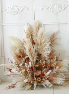 an arrangement of dried flowers and plants in front of a white door