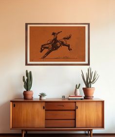 a wooden cabinet with two potted plants on top of it and a framed photo above it