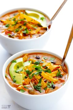 two white bowls filled with soup and topped with avocado