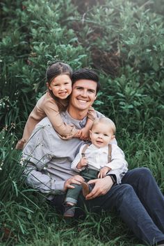 a man and woman are sitting in the grass with their little boy on his lap