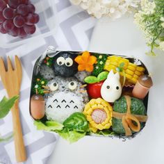 a bento box filled with sushi, vegetables and other food items next to utensils