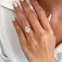 a woman's hand with a diamond ring on her left hand, wearing a white shirt