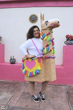 a woman standing next to a fake horse in front of a pink building with decorations on it