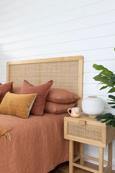 a bed with pillows and blankets on it next to a table with a plant in the corner