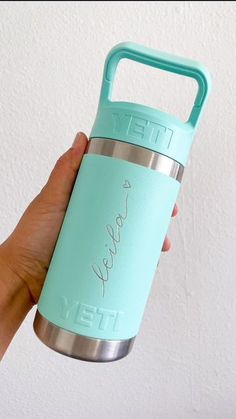 a hand holding a yeti water bottle in front of a white wall with the word yeti written on it