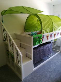 there is a bunk bed with green canopy and storage bins under the stairs in this room