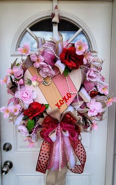 a heart shaped wreath hanging on the front door with pink flowers and pearls around it