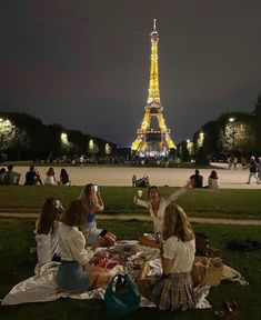 group of people sitting on blanket in front of the eiffel tower at night