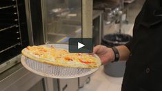 a person holding a pizza in front of an oven with lots of cheese on it