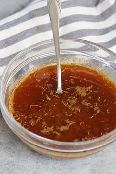 a glass bowl filled with sauce on top of a striped table cloth next to a silver spoon