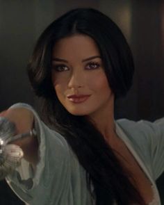 a woman with long black hair holding a silver object in her right hand and looking at the camera