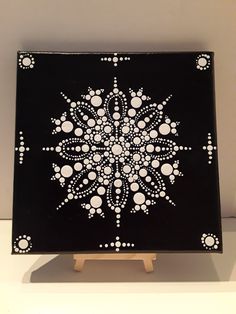 a black and white painting with dots in the shape of a snowflake on a wooden stand