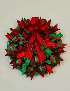 a red and green christmas wreath on a white wall with ribbon attached to the top