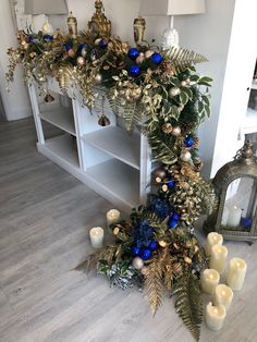 a fireplace decorated with blue and gold christmas decorations, candles and greenery on the mantle