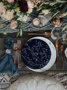 a table setting with place settings, flowers and gold utensils on the side