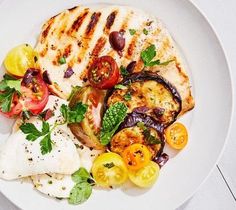 a white plate topped with grilled chicken, tomatoes and other vegtables