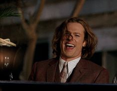 a man in a suit and tie standing next to a potted plant with his mouth open