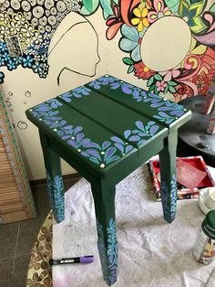 a green stool with blue and purple designs on it, sitting in front of a colorful wall