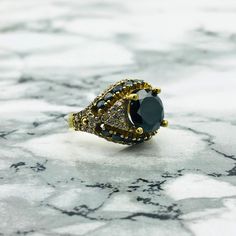 This beautiful Black Onyx ring is a striking piece of craftsmanship that blends elegance with rich detail. The centerpiece features a large, round-cut Black Onyx stone, known for its deep black color and bold presence. Surrounding the Onyx are intricate, curved details that give the ring a vintage-inspired charm. The band is also adorned with smaller stones along the sides, adding to the ring's luxurious and sophisticated look. Handcrafted with care, this ring is perfect for those who appreciate unique and timeless jewelry. Whether for a special event or adding a bold touch to your everyday style, this Black Onyx ring will surely make a statement. Note: Don't forget to visit our store for other color options. Stone Size : 10x10 mm Head Size : 15x20mm  Weight Details: Weighs approximately 6 Black Oval Ring With Black Diamonds, Black Oval Rings With Black Diamonds, Oval Black Rings With Black Diamonds, Elegant Black Cluster Ring As A Gift, Elegant Black Cluster Ring For Promise, Black Sapphire Ring With Black Diamonds As Gift, Gift Black Sapphire Ring With Black Diamonds, Elegant Black Sapphire Ring With Accent Stones, Formal Black Sapphire Ring With Accent Stones