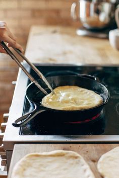 a person is frying food in a skillet on the stove top with two tortillas