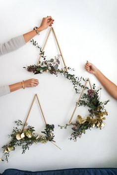 three people holding plants in front of a triangle shaped piece of art that is hanging on the wall