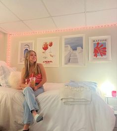 a woman sitting on top of a white bed in a room with pictures above her