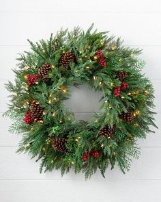 a wreath with pine cones and red berries hanging on a white wall next to a brick wall