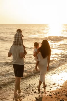 a group of people walking along the beach at sunset with one person carrying a baby