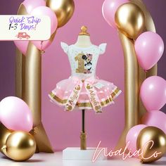 a pink and gold birthday dress on display in front of balloons with the number one