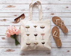 a tote bag sitting on top of a wooden table next to sunglasses and flowers