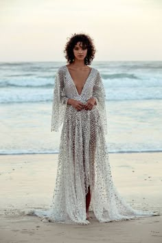 a woman standing on top of a beach next to the ocean wearing a white dress